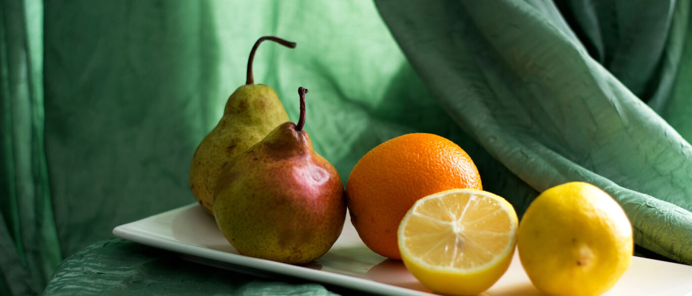 A still-life with fruit Lemon, orange and pears lie on a white ceramic plate on a table
