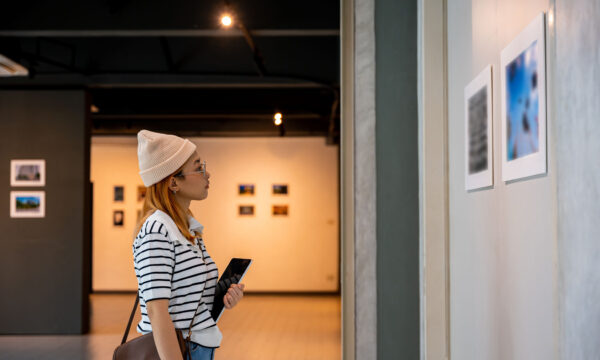 Young person at photo frame hold digital book leaning against at show exhibit artwork gallery Young person at photo frame hold digital book leaning against at show exhibit artwork gallery, Asian woman holding tablet at art gallery collection in front framed paintings looking pictures on wall